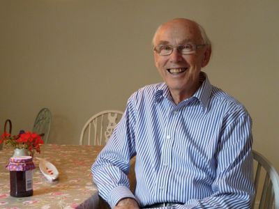 A gentleman in a blue stripy shirt smiling at his breakfast table