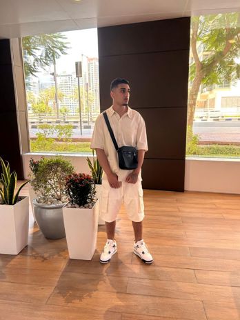 Idris Qayyum wearing a white shirt and shorts with a black cross body bag